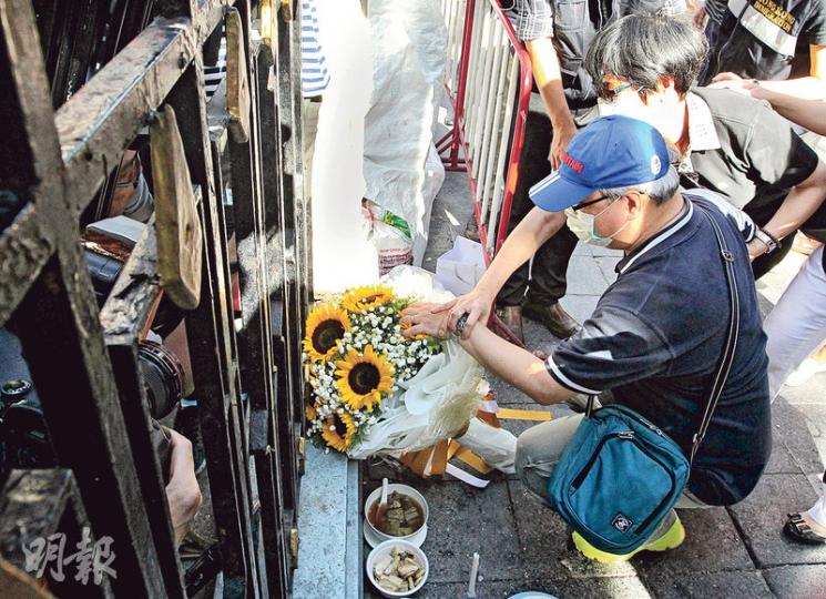 19歲死者陳詠釿的父親（前）帶着一束太陽花到場，其間撫摸花束，低語「快啲返嚟呀，傻豬仔」，淚如泉湧的他由妻子（後）安慰。（林俊源攝） 兩名港人死者家屬昨晨到四面佛爆炸現場拜祭，其中24歲死者彭韻芝的父母（戴口罩者）難抵傷痛，彭母一度伏在丈夫胸前大哭，哭喚女兒「返嚟呀」。（林俊源攝）