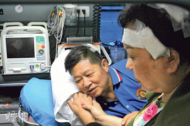 已出院的60歲傷者黃亞娟（右），昨早到醫院會合同樣受傷的62歲丈夫朱日安（左），準備昨午乘飛機回港。她在救護車上陪伴躺在擔架牀上的丈夫，兩人緊握雙手。（林俊源攝）