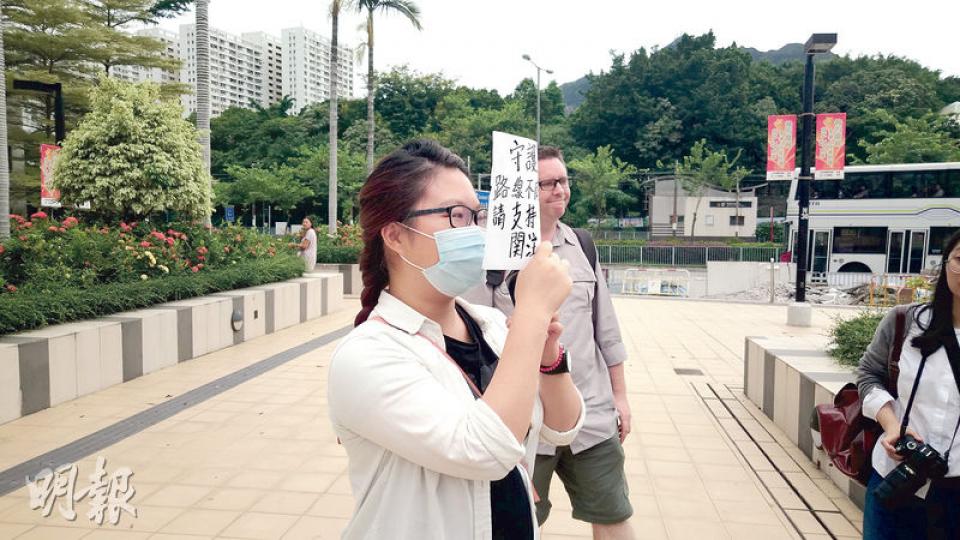 女大學生陳明鳳（戴口罩者）被裁定阻差辦公罪脫後表現興奮， 在庭外以寫有「守護香港」及「路線不同、目標一致」等字句的字牌掩面離開法庭。（張梓鈴攝）