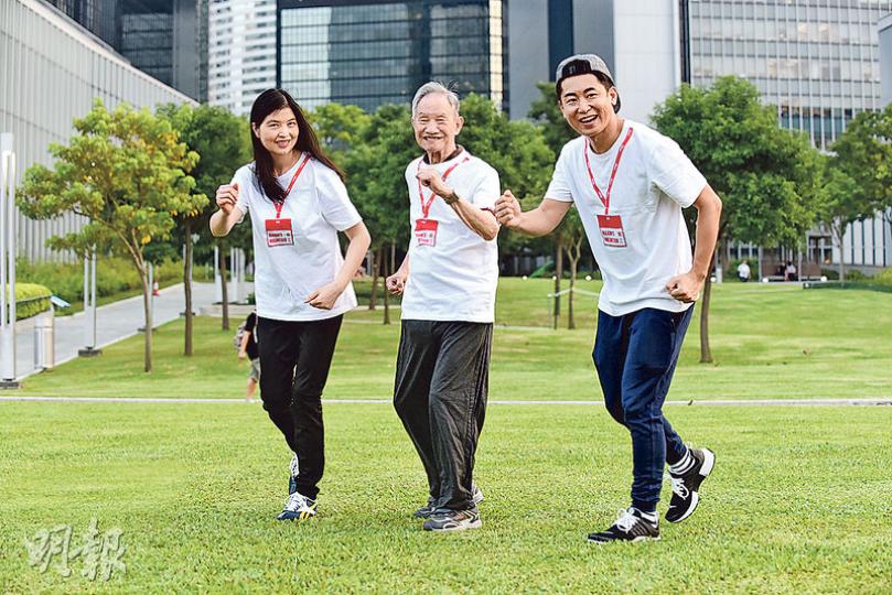 義工Ellis（右）與Funky（左）陪同88歲長者李文（中）一起到添馬公園練跑。李伯在安老院中不苟言笑，但到公園後即笑逐顏開。李伯說自己平日很少外出，但其實很喜歡活動，能出來練跑感到開心。 （陳淑安攝）