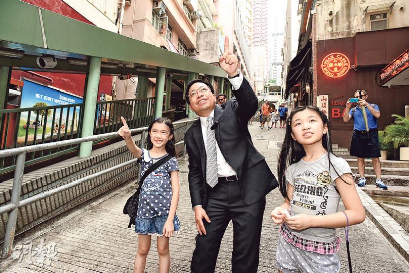 香港測量師學會會長何鉅業親自帶小朋友認識今日的中區面貌。（陳淑安攝）平日我們使用中區行人扶手電梯，只知道它很長很長，其實它是帶動中半山發展的重要建設，令中區SOHO應運而生。細心留意，我們乘搭電梯時，可看到位於樓宇一、二層各式商舖，原來電梯令它們更易被發現，也就增加了它們的商機！（陳淑安攝）不經不覺，我們花數分鐘便經行人天橋由上環走至中環。行人天橋可做到人車分流，也可連貫主要建築物，是城巿發展中不可或缺的。（陳淑安攝）測量師何鉅業指中區新舊樓宇交替，甚具特色，然而為何不能全部一起重建呢？原來要考