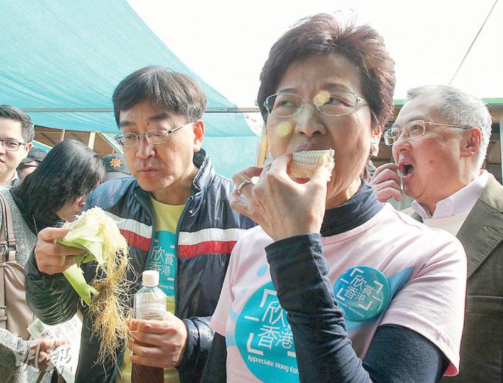 政務司長林鄭月娥（中）及食物及衛生局長高永文（左）昨到漁農美食迎春嘉年華主持典禮，並到其中一間有機農場攤檔購買甜粟，更即場生吃粟米。高永文其後表示，粟米十分甜。（李紹昌攝）