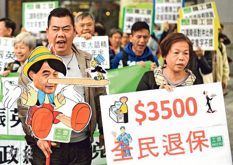 關注綜援低收入聯盟率近200人遊行，不少遊行者帶同標語，諷刺政府遲遲不落實全民退保方案。（蘇智鑫攝）