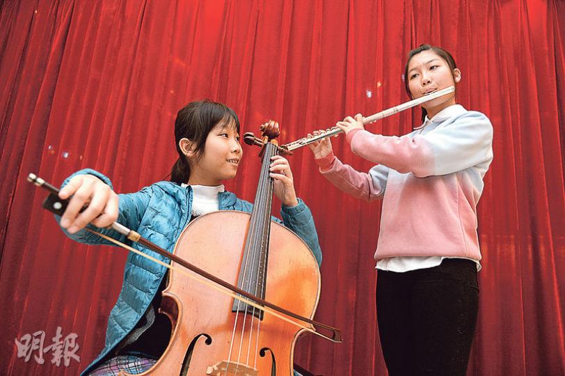妹妹李雪庭（左）的大提琴為是次樂器回收活動中所得樂器，「音樂兒童基金」先把樂器翻新和調音，再與合適的兒童配對，雪庭很可能獲贈她手中這把大提琴。姊姊雪蓮（右）手中的長笛屬於基金會，只限在中心內使用。（鍾林枝攝）