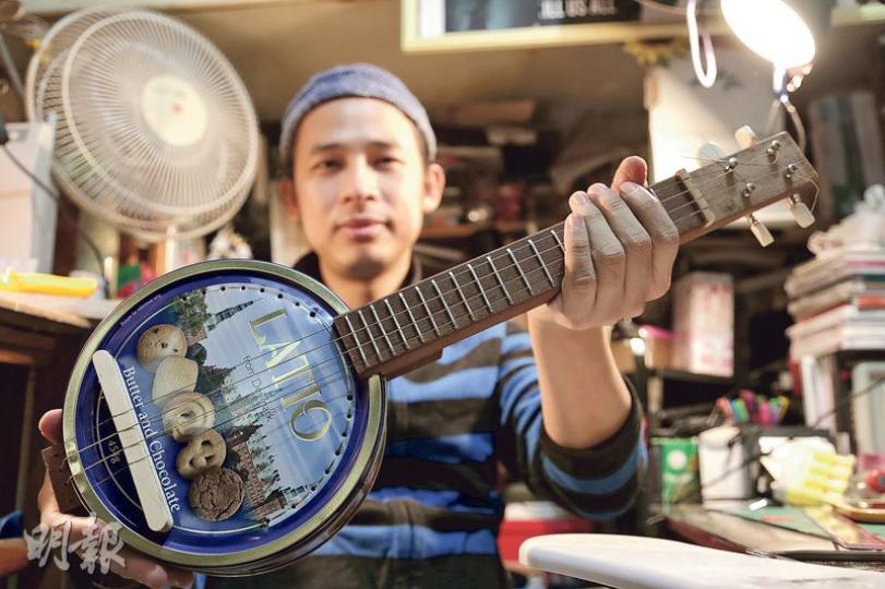 愛彈結他的卓翹（圖）利用廢木和鐵罐，手製夏威夷小結他（Ukulele），至今做了8支，他手中的是特意為訪問而做的最新作品。（周智堅攝）圖左的黑色摺枱完好無缺，只是木板較骯髒、金屬部件生鏽，修理後應可重用。卓翹會留意可有合用的木方製作環保結他頸，例如他手中的木方就是在這垃圾站拾獲。（楊柏賢攝）