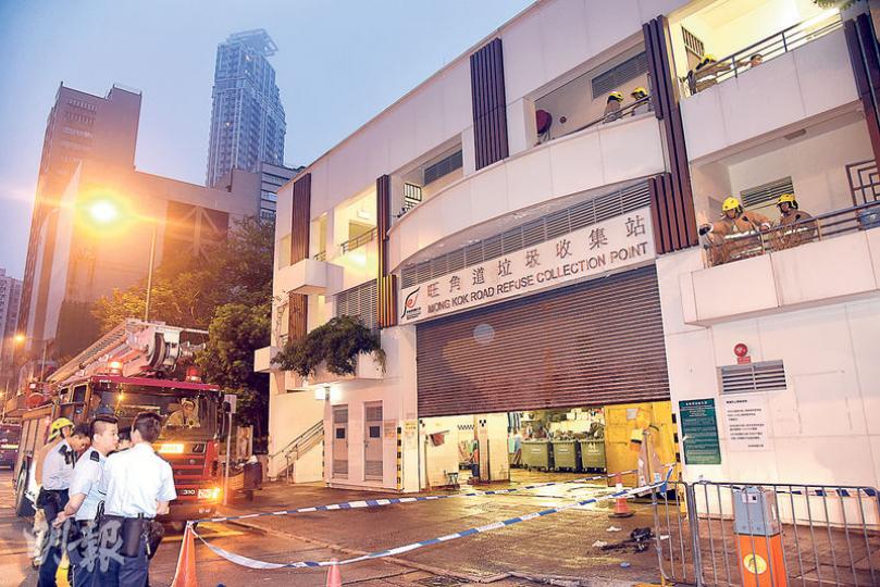 警方及消防封鎖案發的垃圾站調查。自焚男子相信是從圖中右邊垃圾站頂層（二樓）位置墮下。（蔡方山攝）消防員在場使用探測儀器檢查死者遺下的燒焦衣物碎片，以調查火警起因。（蔡方山攝）