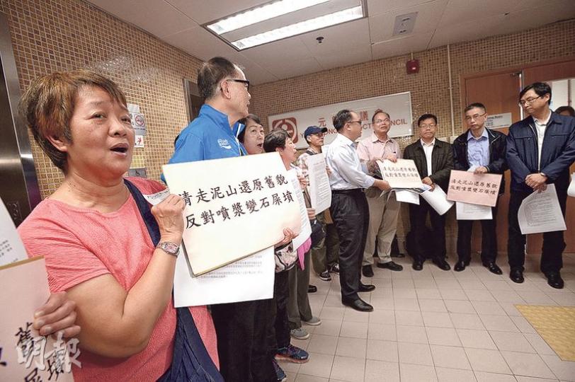 元朗區議會昨召開特別會議討論天水圍泥頭山事件，10多名嘉湖山莊居民在門外示威，反對泥頭山噴漿，憂變成「石屎山墳」破壞景觀。元朗區議員李月民（白衫黑褲者）向政府代表遞交請願信，要求為泥頭山綠化。（楊柏賢攝）