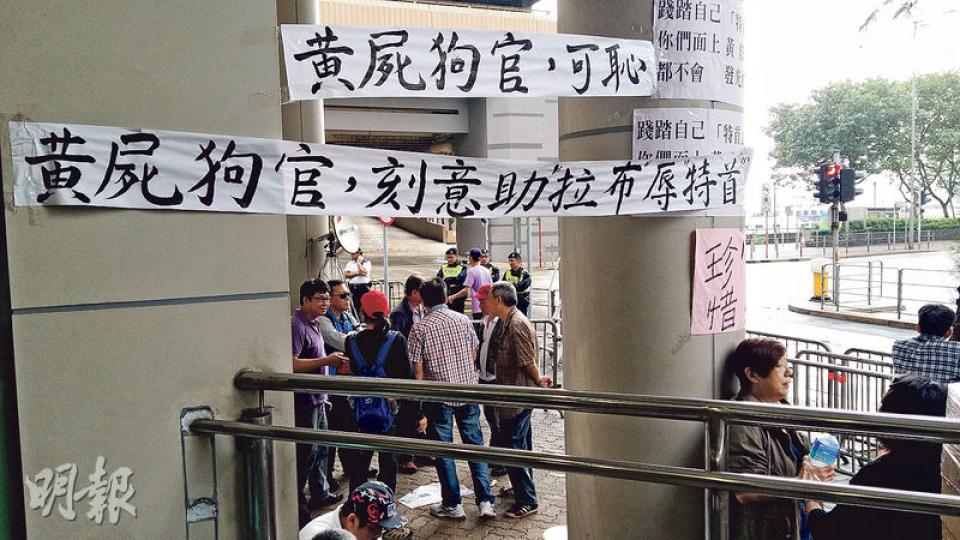 昨有人在東區法院門外掛起「黃屍狗官，刻意助拉布辱特首」標語。珍惜群組召集人李璧而回覆本報查詢時承認標語出自他們手筆，稱法官在庭上容許黃毓民如此囂張，反問「個法官係咪有問題？」但李後來又稱，群組組織鬆散，不知標語是誰掛上。（鄧力行攝）大批梁振英支持者昨到法院外示威，其間有人高舉國旗及區旗於法院外巡行，卻將國旗倒轉掛。（黃建邦攝）