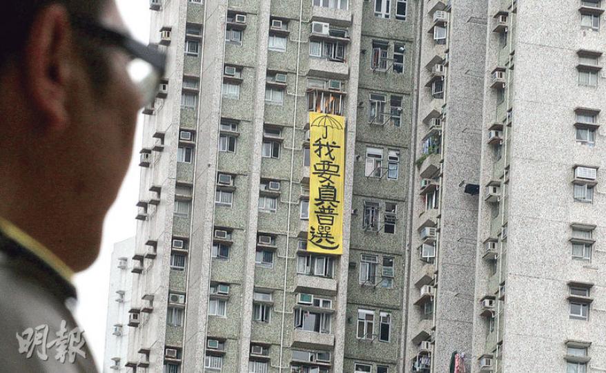 張德江到訪將軍澳的安老院期間,社民連於對面的欣明苑一座大廈窗外,掛上3層樓高的「我要真普選」黃色巨型直幡,上面畫有雨傘圖案。(李紹昌攝) 張德江到訪將軍澳的安老院期間,社民連於對面的欣明苑一座大廈窗外,掛上3層樓高的「我要真普選」黃色巨型直幡,上面畫有雨傘圖案。(李紹昌攝)
