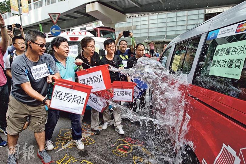 參與遊行的士車身張貼反對標語,其後的士業界代表用貼上「混房局」標語的水桶向一部優質的士潑水,象徵運房局漠視業界反對聲音,向現有優質的士潑冷水。(李紹昌攝) 參與遊行的士車身張貼反對標語,其後的士業界代表用貼上「混房局」標語的水桶向一部優質的士潑水,象徵運房局漠視業界反對聲音,向現有優質的士潑冷水。(李紹昌攝)