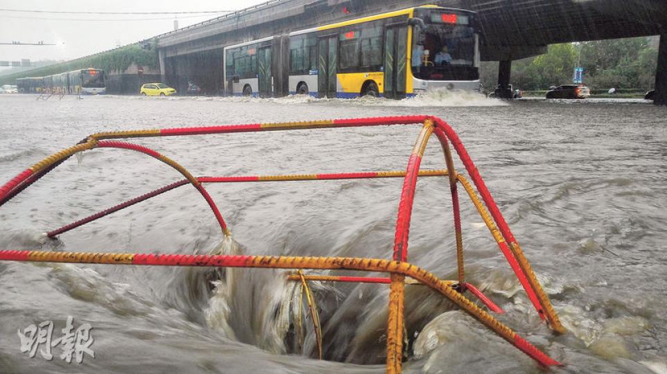 北京昨日下暴雨，路政人員掀開一處渠蓋以利排水，並放置鐵架在旁防止有人誤墮。（鄭海龍攝）北京豐台區西紅門橋因嚴重水浸，社區工作人員冒雨站在路中央阻止車輛進入積水路段。（鄭海龍攝）