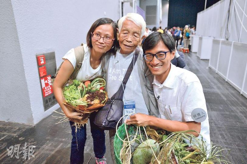 朱凱廸(右)一直推動「民主自決,城鄉共生」,當年有份參與反對清拆菜園村運動,與村民關係深厚。89歲菜園村村民高婆婆(中)昨早4時起牀,乘的士到點票中心撐場,當知道朱凱廸獲得逾8萬票時表現雀躍,大呼「我好開心呀」,並送了一籃自家種蔬菜給他。左為朱凱廸妻子。(鍾林枝攝) 朱凱廸(右)一直推動「民主自決,城鄉共生」,當年有份參與反對清拆菜園村運動,與村民關係深厚。89歲菜園村村民高婆婆(中)昨早4時起牀,乘的士到點票中心撐場,當知道朱凱廸獲得逾8萬票時表現雀躍,大呼「我好開心呀」,並送了一籃自家種蔬菜給他。左為朱凱廸妻子。(鍾林枝攝)