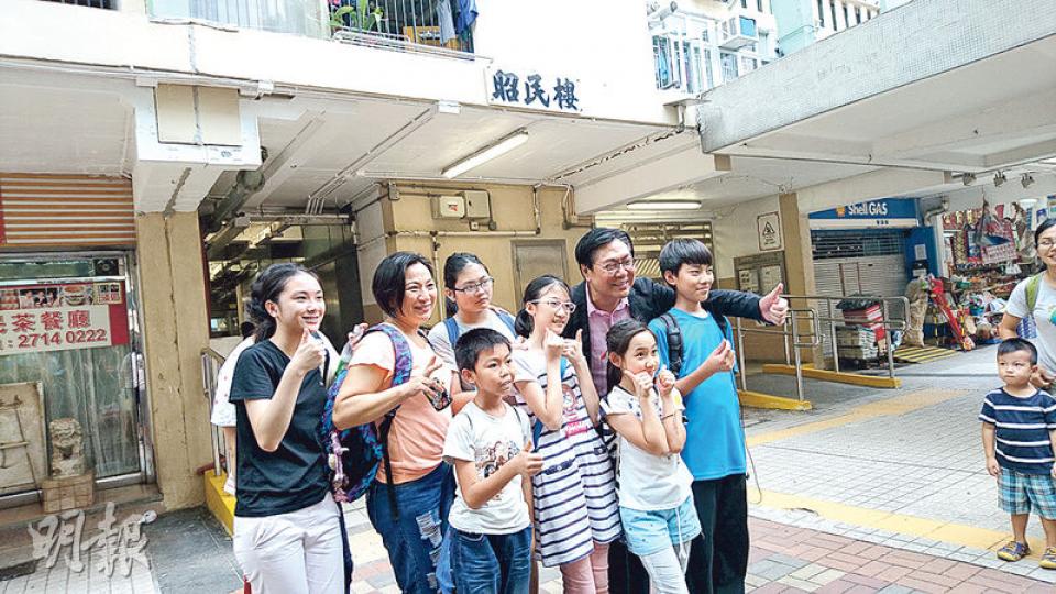 馬時亨（後右二）話，逾40年前住過愛民邨昭民樓，當時上到樓嘅興奮同噚日觀塘延線通車一樣。佢重遊舊地，吸引咗唔少街坊同佢合照，佢又沿途問啲街坊有冇試搭新港鐵站。（岑詠欣攝）