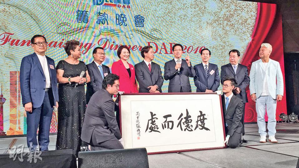 民建聯舉行籌款晚宴，中聯辦主任張曉明（後排右四）嘅「度德而處」書法，由無出席晚宴嘅全國政協高敬德電話遙控代表以1880萬元投得，張主任特別強調自己無從中取得一分錢。拍賣環節有藝人陳百祥（右一）及肥媽Maria（左二）協助。（何曉勤攝）民建聯前主席譚耀宗（左）同主席李慧琼（右）合唱《東方之珠》好投入，做晒動作，為民記籌得500萬元。（何曉勤攝）前年以1380萬投得張曉明書法嘅全國政協委員許榮茂（中），今次以300萬元投得饒宗頤寫嘅「上善若水」。（何曉勤攝）有張德江親筆簽名嘅《基本法》，由全國政協委