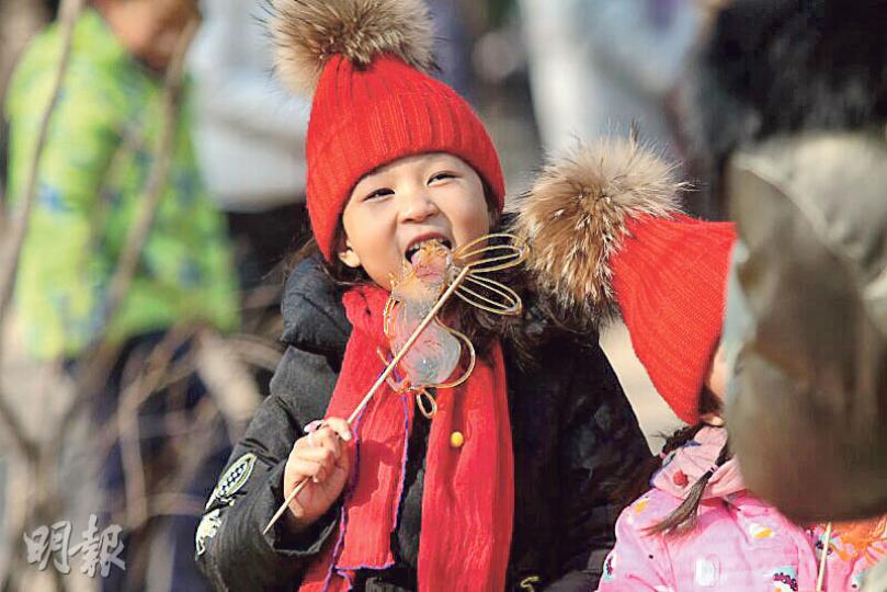 在廟會上,一個小女孩在得到糖畫兒後,迫不及待地吃了起來。(鄭海龍攝) 在廟會上,一個小女孩在得到糖畫兒後,迫不及待地吃了起來。(鄭海龍攝)