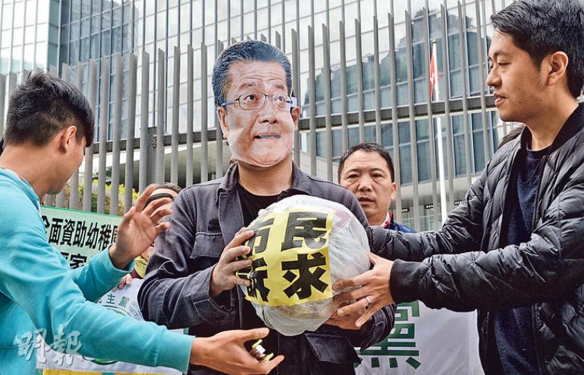 有民主黨員昨在請願中戴上新任財政司長陳茂波的面具(中),促請對方在預算案回應市民訴求,善用財政盈餘。(劉焌陶攝) 有民主黨員昨在請願中戴上新任財政司長陳茂波的面具(中),促請對方在預算案回應市民訴求,善用財政盈餘。(劉焌陶攝)