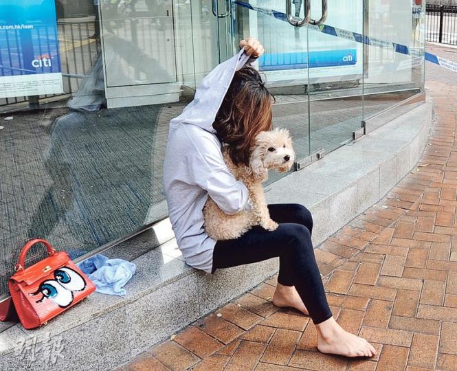 東海大廈火警期間，有住戶帶着愛犬和手袋逃生，事後赤腳坐在路邊石壆等候解封回家。（衛永康攝）