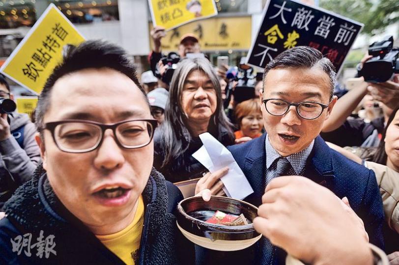 人民力量副主席譚得志（左）、社民連梁國雄（中）等亦到場外示威，反對中央欽點特首，有示威者帶咗放上500元現金嘅「乞兒兜」，諷刺林太施捨500元畀乞丐一事。其間保安鎖上麥花臣場館正門，林太競選辦人員、民建聯嘅張國鈞（右）亦被示威者包圍。（馮凱鍵攝）