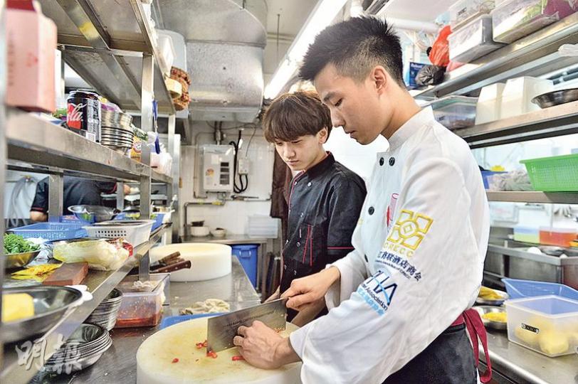 年僅24歲的大廚黃飛(白衣者)希望培養更多90後年輕人入行,訪問當日一名學徒(黑衣者)第3日上班,黃飛說對方20歲,也是新移民,很願意學習,令他好像看到當年的自己。圖為黃飛向學徒示範切辣椒。(鄧宗弘攝) 年僅24歲的大廚黃飛(白衣者)希望培養更多90後年輕人入行,訪問當日一名學徒(黑衣者)第3日上班,黃飛說對方20歲,也是新移民,很願意學習,令他好像看到當年的自己。圖為黃飛向學徒示範切辣椒。(鄧宗弘攝)