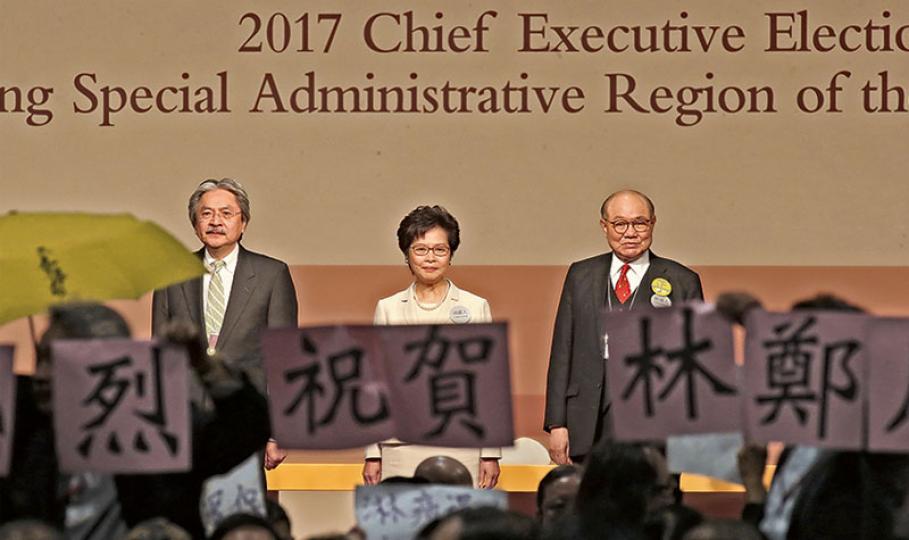 第五屆特首選舉昨日舉行,林鄭月娥(中)以777票當選,落敗的曾俊華(左)及胡國興(右)則分別取得365票及21票。3人在台上期間,台下有部分民主派選委舉黃傘抗議,而漁農界選委即拿着祝賀林太當選字句的標語走到台前中央位置舉起。(曾憲宗攝) 第五屆特首選舉昨日舉行,林鄭月娥(中)以777票當選,落敗的曾俊華(左)及胡國興(右)則分別取得365票及21票。3人在台上期間,台下有部分民主派選委舉黃傘抗議,而漁農界選委即拿着祝賀林太當選字句的標語走到台前中央位置舉起。(曾憲宗攝)