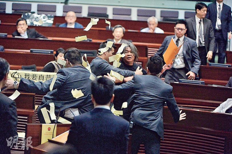 社民連梁國雄昨多次提規程問題,質疑建制派「揼波鐘」,中途又衝向特首梁振英撒溪錢,並撕爛施政報告,批評梁振英迴避UGL問題及全民退保,部分溪錢散落梁振英的桌面。梁國雄隨即被多重保安包圍(圖),並在主席梁君彥要求下被帶離場。(馮凱鍵攝) 社民連梁國雄昨多次提規程問題,質疑建制派「揼波鐘」,中途又衝向特首梁振英撒溪錢,並撕爛施政報告,批評梁振英迴避UGL問題及全民退保,部分溪錢散落梁振英的桌面。梁國雄隨即被多重保安包圍(圖),並在主席梁君彥要求下被帶離場。(馮凱鍵攝)