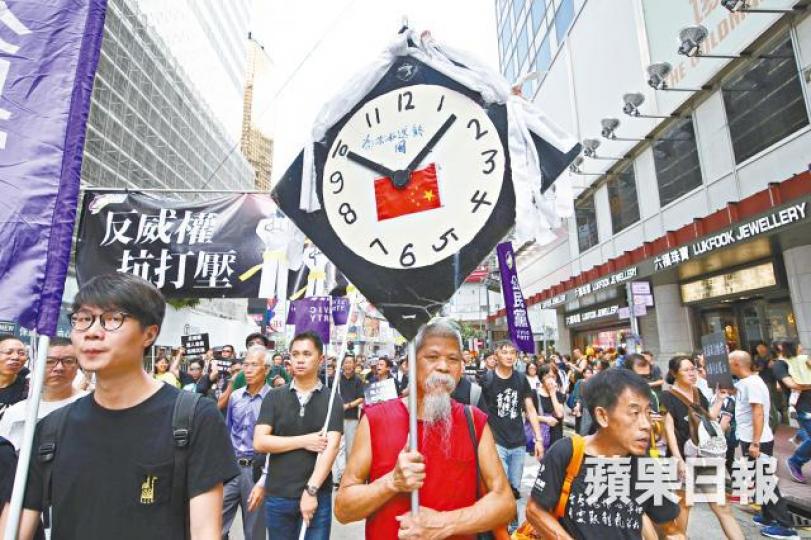 ■古思堯高舉時鐘形狀的示威道具，稱「為共和國送終」。馬泉崇攝