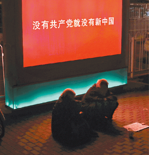 ■北京到處展示政治標語,一對老人在屏幕前行乞。美聯社
■北京到處展示政治標語,一對老人在屏幕前行乞。美聯社