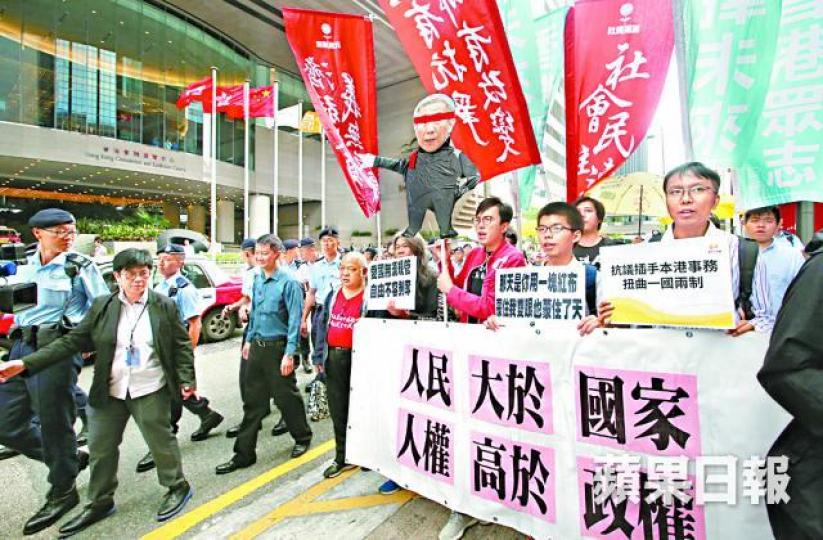 ■社民連及眾志昨持雙眼矇着紅巾的李飛紙版公仔於會場外遊行。馬泉崇攝■大批警員一度包圍遊行人士阻止示威。 ■社民連及眾志昨持雙眼矇着紅巾的李飛紙版公仔於會場外遊行。馬泉崇攝■大批警員一度包圍遊行人士阻止示威。