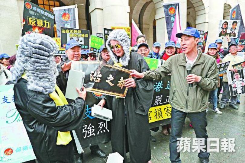 ■保衛香港運動傅振中(右一)昨與扮成法官的撐警人士,打爛印有「法治之都」的道具。張志華攝 ■保衛香港運動傅振中(右一)昨與扮成法官的撐警人士,打爛印有「法治之都」的道具。張志華攝
