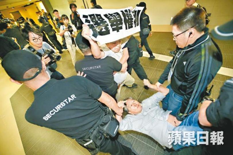 李卓人高舉標語抗議後,被3名保安粗暴抬離現場。黎樹雄攝選舉主任郭偉勳 李卓人高舉標語抗議後,被3名保安粗暴抬離現場。黎樹雄攝選舉主任郭偉勳