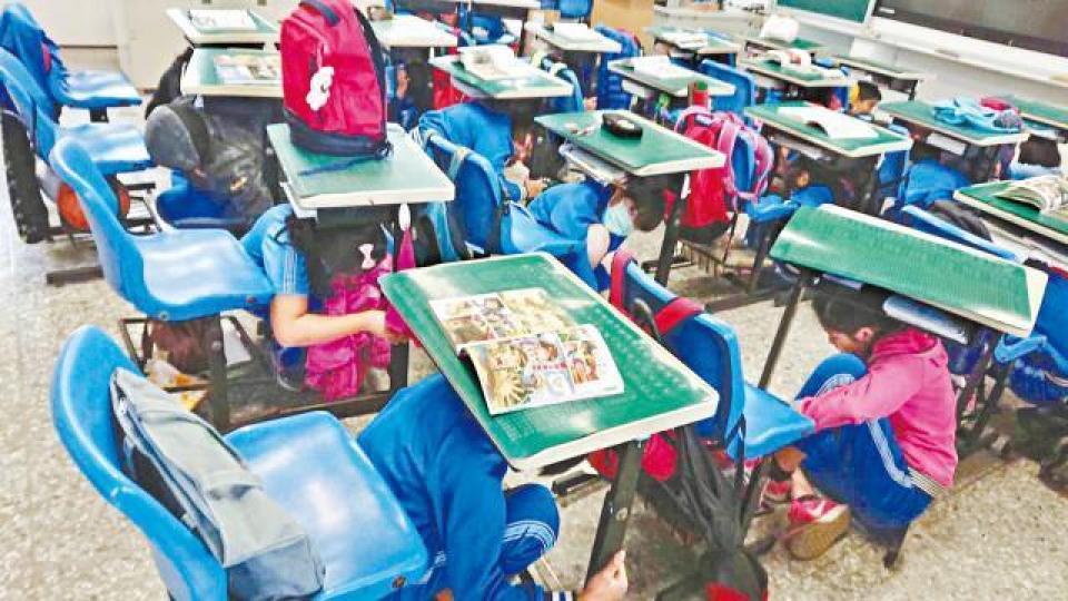 金門一小學的教師教導小孩躲枱底。 金門一小學的教師教導小孩躲枱底。