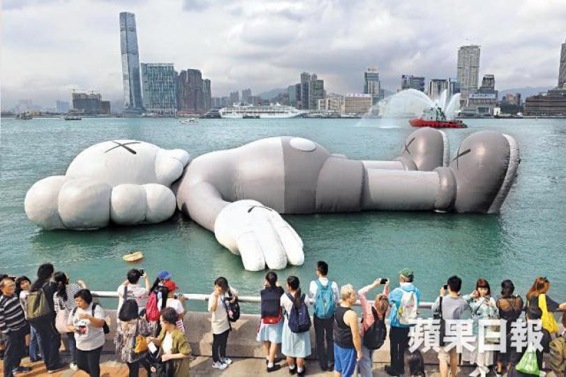 COMPANION昨日抵達添馬公園對出海面展出,滅火輪「精英號」作噴水表演「助興」。朱永倫攝KAWS(左)及策展人林樹鑫。COMPANION一度洩氣,大會解釋展品需放氣換電,換電後已即時再充氣。展出首天已吸引不少人往「打卡」。以放鬆姿態仰卧維港海面望向天空的COMPANION,寓意希望港人像COMPANION一樣抽時間躺下,看看天空放鬆一下。 COMPANION昨日抵達添馬公園對出海面展出,滅火輪「精英號」作噴水表演「助興」。朱永倫攝KAWS(左)及策展人林樹鑫。COMPANION一度洩氣,大會解釋展品需放氣換電,換電後已即時再充氣。展出首天已吸引不少人往「打卡」。以放鬆姿態仰卧維港海面望向天空的COMPANION,寓意希望港人像COMPANION一樣抽時間躺下,看看天空放鬆一下。